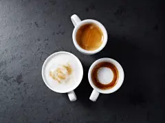 Trzy białe filiżanki z kawą: espresso, latte macchiato i kawą z pianką na ciemnym tle.