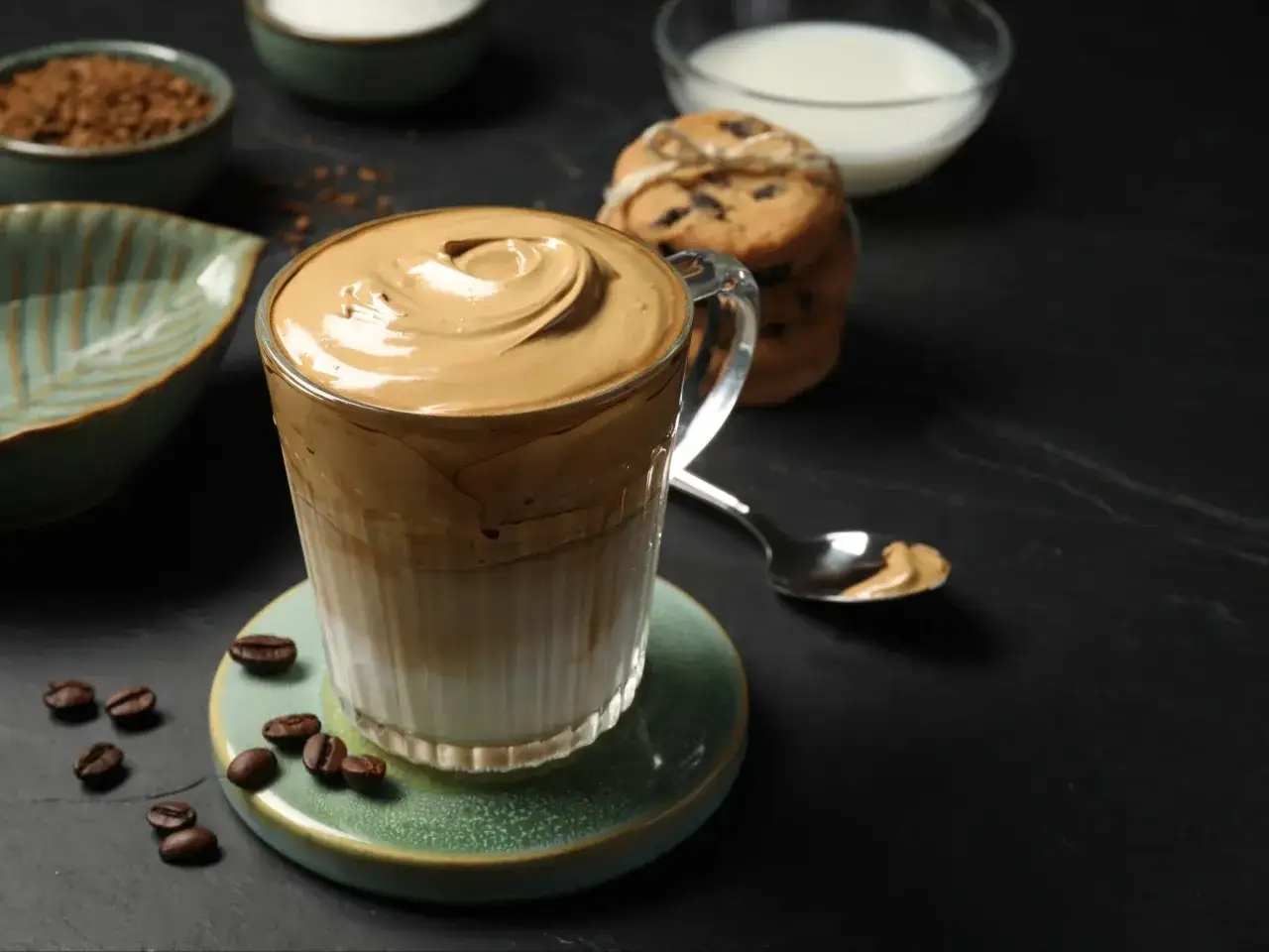 Puszysty, kremowy dalgona coffee w szklance, obok ciasteczka i ziarenka kawy. Idealny na chwilę relaksu.