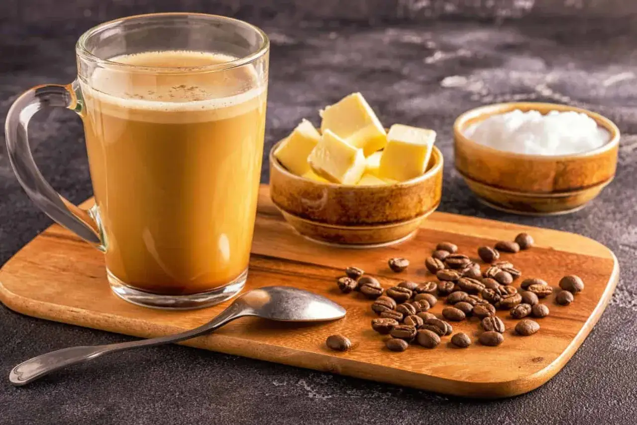 Kawa kuloodporna (bullet coffee) w szklance, obok miseczki z masłem, cukrem i ziarnami kawy.